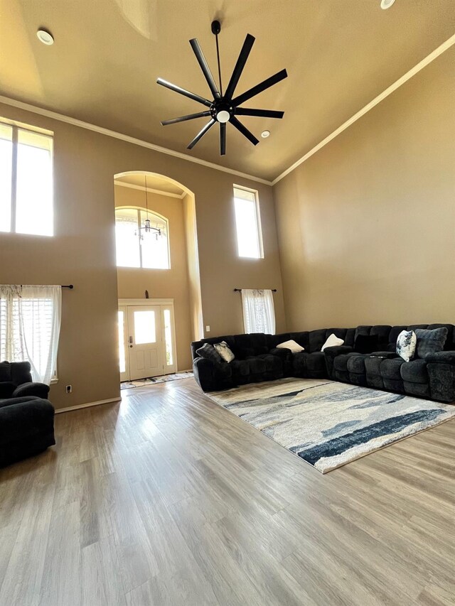 living room featuring a notable chandelier, ornamental molding, a high ceiling, and light wood-type flooring