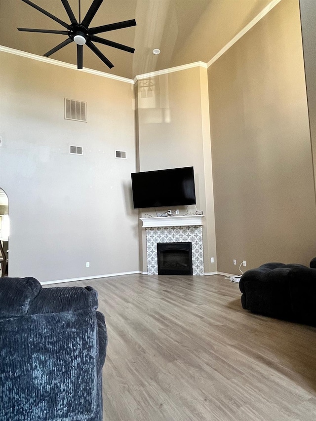 living room with a tile fireplace, crown molding, wood-type flooring, and ceiling fan