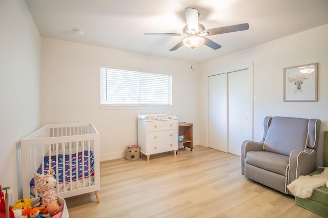 bedroom featuring a crib, ceiling fan, light hardwood / wood-style floors, and a closet