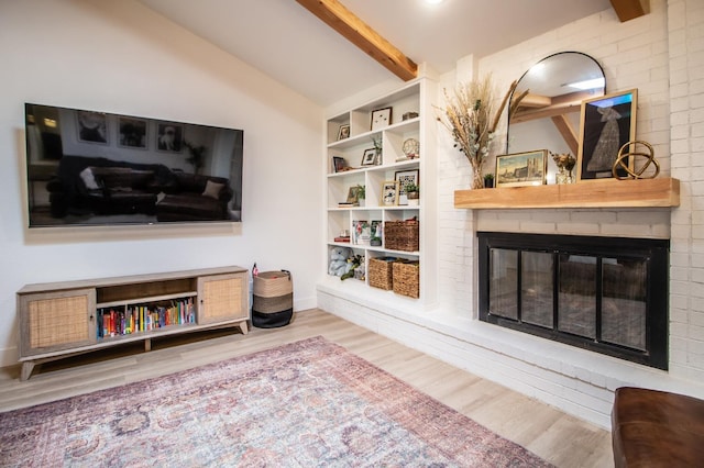 living room with lofted ceiling with beams, a brick fireplace, and light hardwood / wood-style flooring