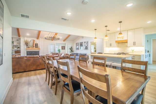 dining space featuring vaulted ceiling with beams, a chandelier, and light wood-type flooring