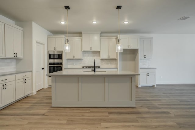 kitchen featuring hanging light fixtures, appliances with stainless steel finishes, a kitchen island with sink, and light wood-type flooring