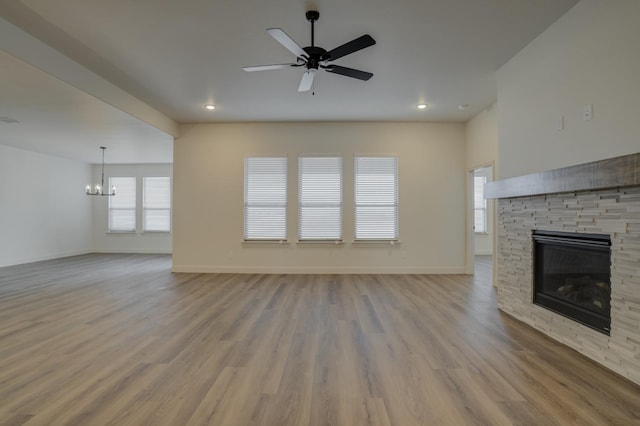 unfurnished living room featuring ceiling fan with notable chandelier, a fireplace, and light hardwood / wood-style floors