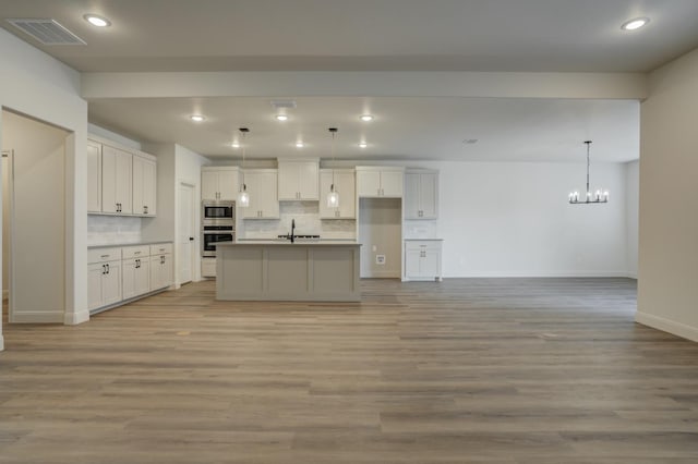 kitchen featuring appliances with stainless steel finishes, white cabinetry, backsplash, light hardwood / wood-style floors, and a center island with sink