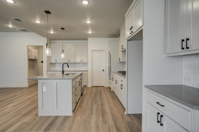 kitchen featuring white cabinetry, sink, pendant lighting, and an island with sink