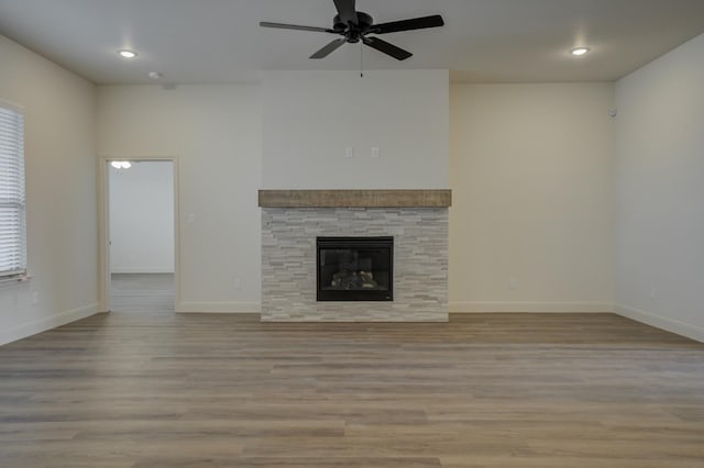 unfurnished living room featuring ceiling fan, a stone fireplace, a healthy amount of sunlight, and light wood-type flooring