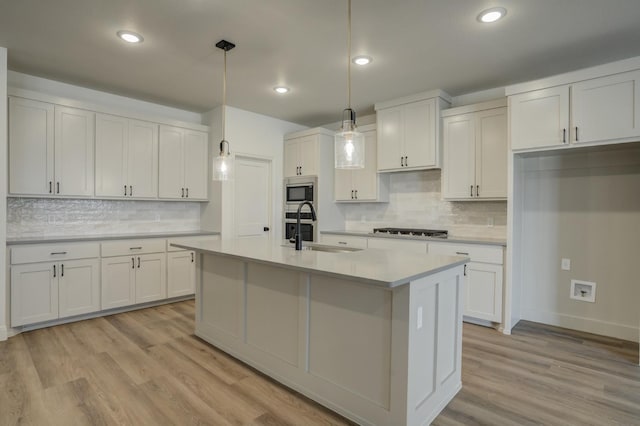 kitchen with sink, white cabinetry, hanging light fixtures, appliances with stainless steel finishes, and light hardwood / wood-style floors