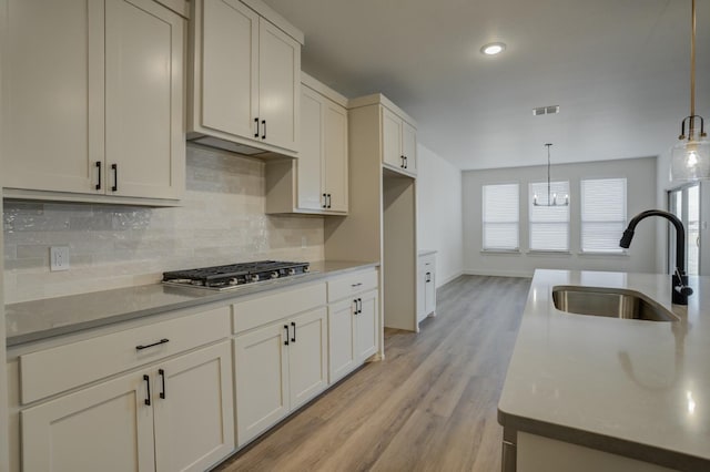 kitchen with sink, decorative light fixtures, light hardwood / wood-style flooring, stainless steel gas stovetop, and decorative backsplash