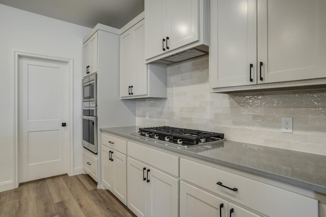 kitchen with tasteful backsplash, stainless steel appliances, light wood-type flooring, and white cabinets