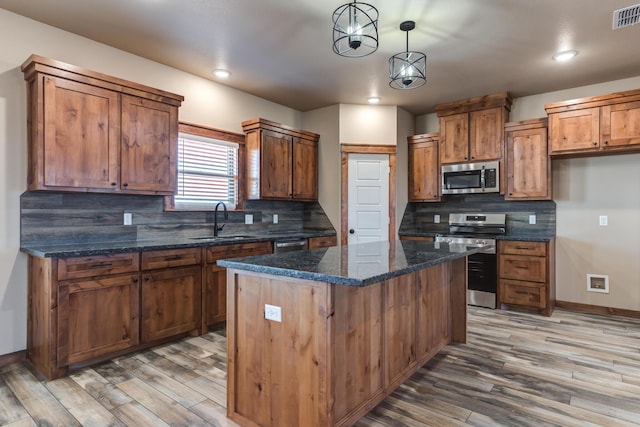 kitchen with stainless steel appliances, a sink, a kitchen island, brown cabinets, and pendant lighting