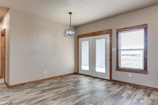 unfurnished room featuring a chandelier, baseboards, and wood finished floors