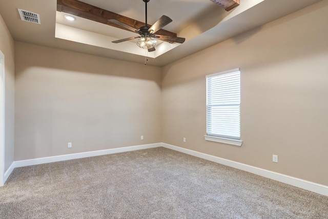 carpeted spare room with a ceiling fan, a raised ceiling, visible vents, and baseboards