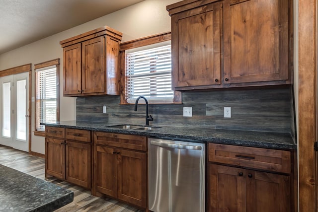 kitchen with plenty of natural light, decorative backsplash, dark stone counters, stainless steel dishwasher, and a sink