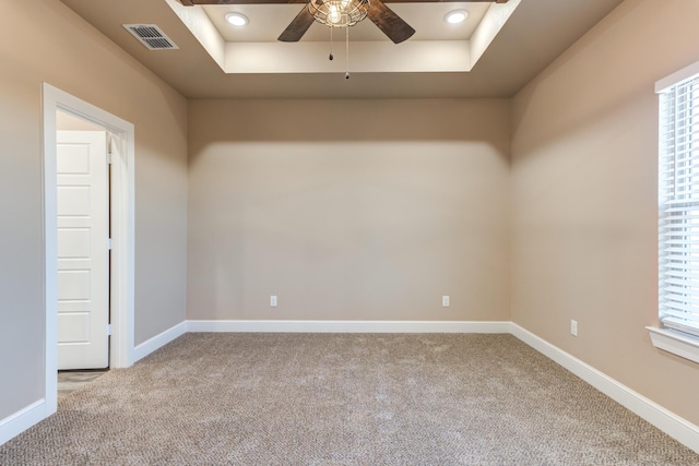 carpeted spare room featuring a tray ceiling, a ceiling fan, visible vents, and baseboards