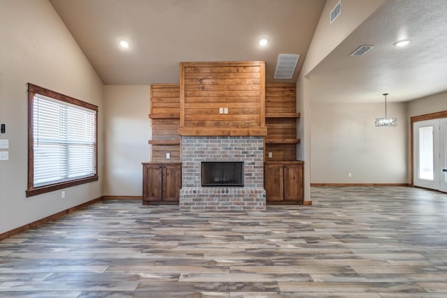 unfurnished living room featuring a brick fireplace, plenty of natural light, and visible vents