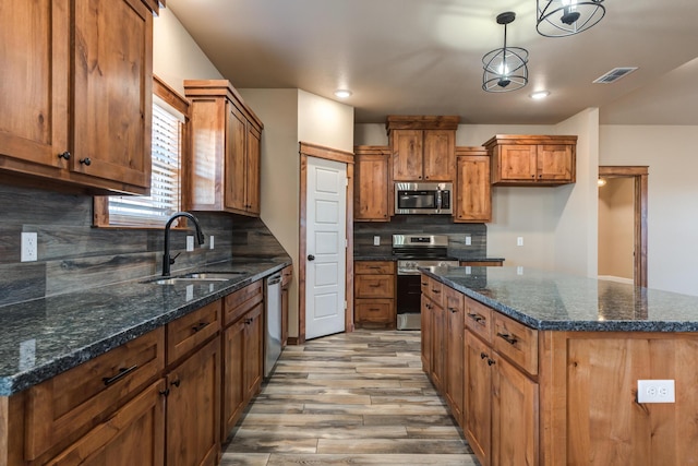 kitchen with brown cabinets, stainless steel appliances, hanging light fixtures, a sink, and a kitchen island