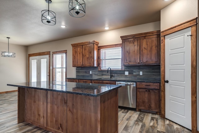 kitchen featuring a sink, hanging light fixtures, a center island, dishwasher, and dark stone countertops