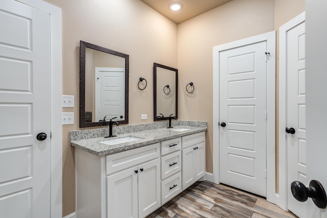 bathroom with double vanity, baseboards, a sink, and wood finished floors