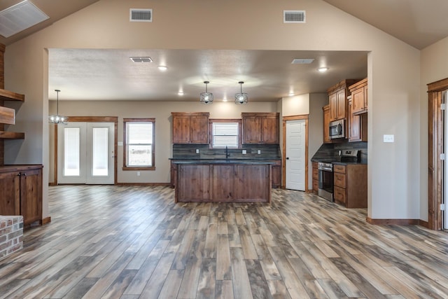 kitchen featuring brown cabinets, tasteful backsplash, dark countertops, hanging light fixtures, and appliances with stainless steel finishes