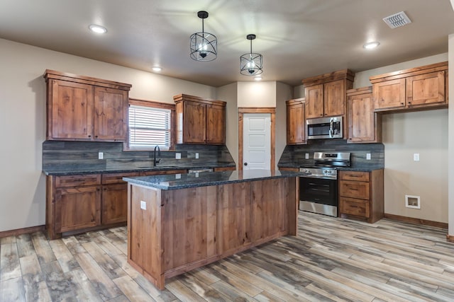 kitchen with visible vents, brown cabinetry, appliances with stainless steel finishes, a center island, and a sink