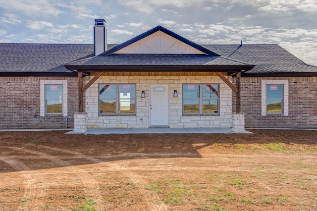 view of front of house featuring a patio, a shingled roof, a chimney, and brick siding