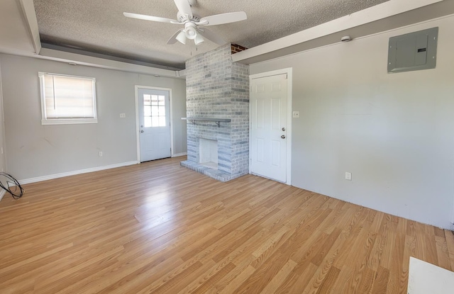 unfurnished living room with a fireplace, electric panel, ceiling fan, light hardwood / wood-style floors, and a textured ceiling