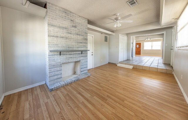 unfurnished living room featuring ceiling fan, a fireplace, light hardwood / wood-style floors, and a textured ceiling