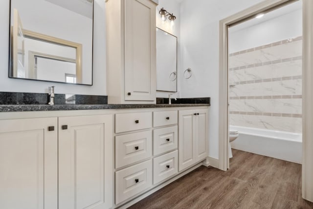 full bathroom with wood-type flooring, tiled shower / bath, vanity, and toilet