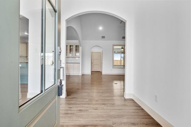 corridor featuring light wood-type flooring, baseboards, and arched walkways