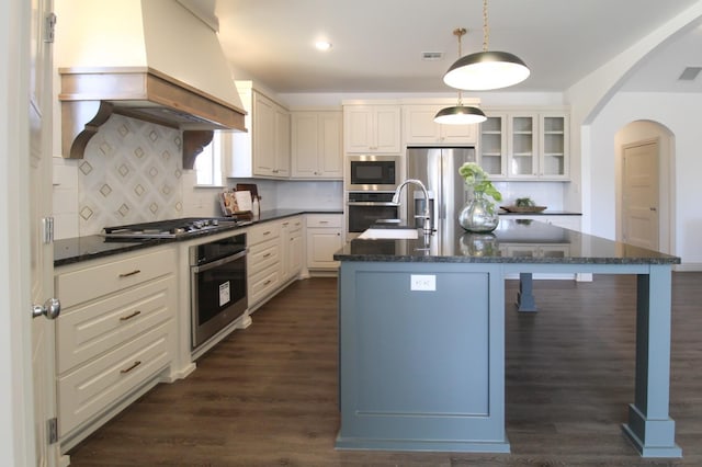 kitchen featuring a breakfast bar area, custom exhaust hood, appliances with stainless steel finishes, pendant lighting, and a kitchen island with sink