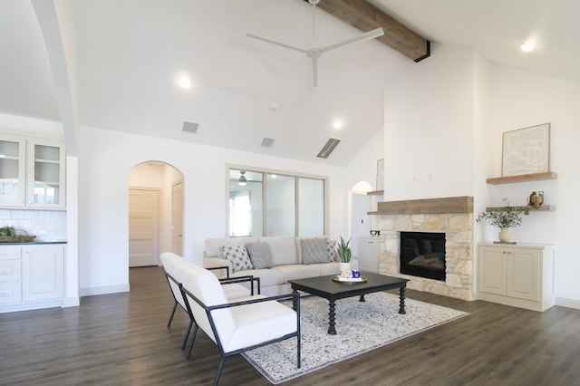 living room featuring beamed ceiling, a stone fireplace, dark hardwood / wood-style floors, and ceiling fan