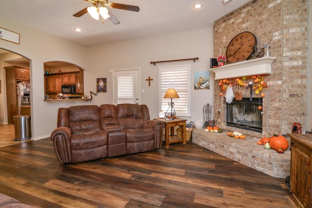 living room with dark wood-type flooring, ceiling fan, and a fireplace