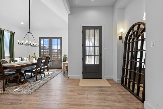 foyer featuring french doors, a towering ceiling, a chandelier, and light hardwood / wood-style flooring