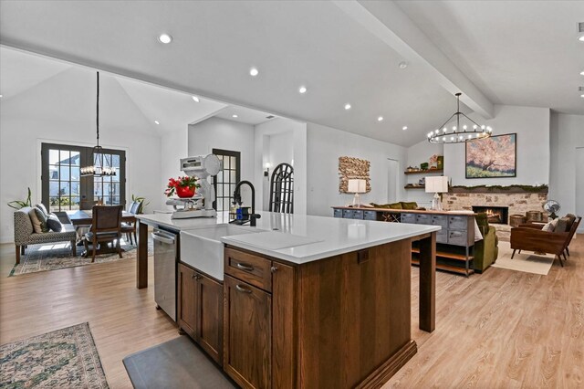 kitchen featuring a stone fireplace, decorative light fixtures, a center island with sink, stainless steel dishwasher, and a notable chandelier