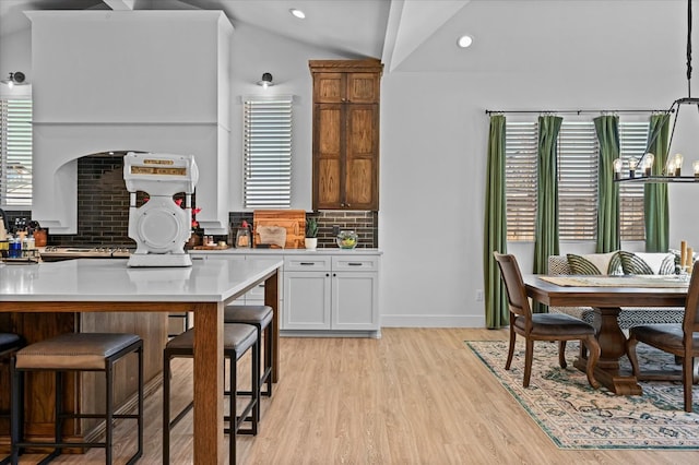 kitchen with lofted ceiling, white cabinetry, a chandelier, light hardwood / wood-style floors, and decorative backsplash