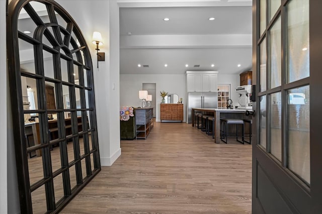 hallway with sink, light hardwood / wood-style flooring, and beamed ceiling