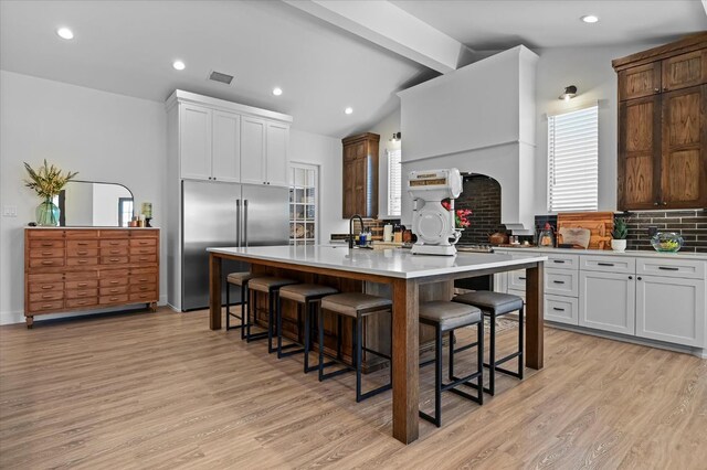 kitchen with stainless steel built in refrigerator, a breakfast bar, a center island with sink, and white cabinets