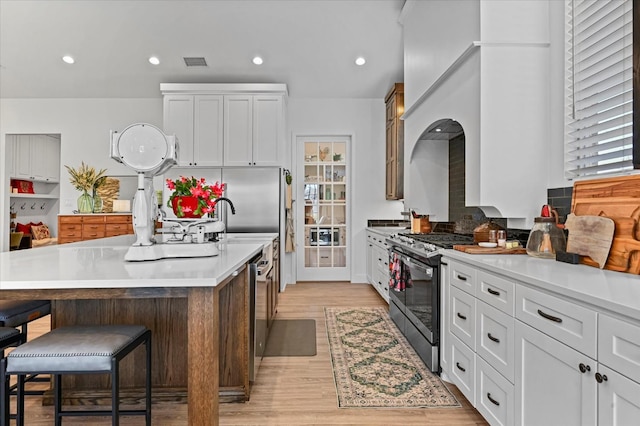 kitchen with appliances with stainless steel finishes, a kitchen island with sink, white cabinets, a kitchen bar, and light wood-type flooring