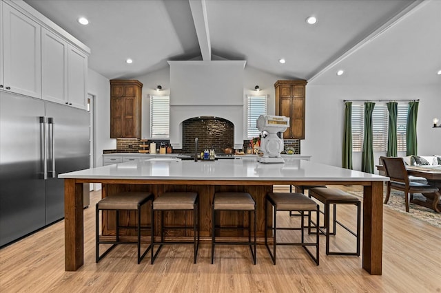 kitchen with a spacious island, vaulted ceiling with beams, white cabinetry, stainless steel built in fridge, and light hardwood / wood-style floors