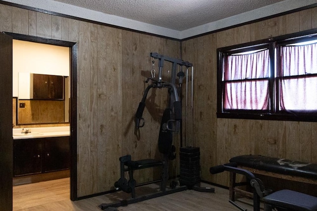 exercise room with sink, wood walls, a textured ceiling, and light wood-type flooring