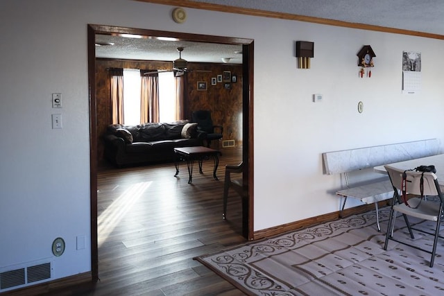 hallway featuring wood-type flooring, a textured ceiling, crown molding, and wood walls