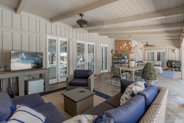 living room with beamed ceiling, ceiling fan with notable chandelier, french doors, and wood walls