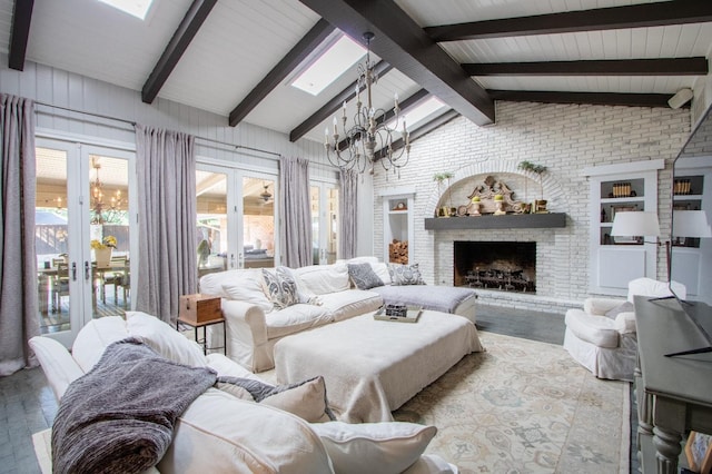 living room featuring vaulted ceiling with skylight, a notable chandelier, a fireplace, built in shelves, and french doors