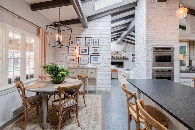 dining space featuring brick wall, high vaulted ceiling, a fireplace, beamed ceiling, and a chandelier