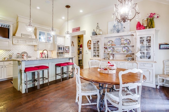 dining area with dark wood-type flooring, lofted ceiling, sink, an inviting chandelier, and ornamental molding