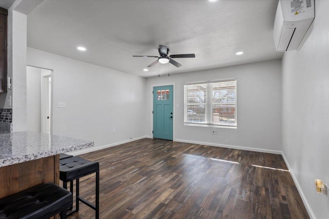 interior space with baseboards, dark wood-type flooring, an AC wall unit, and recessed lighting