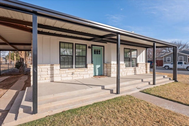 view of front of property with board and batten siding, stone siding, covered porch, and fence