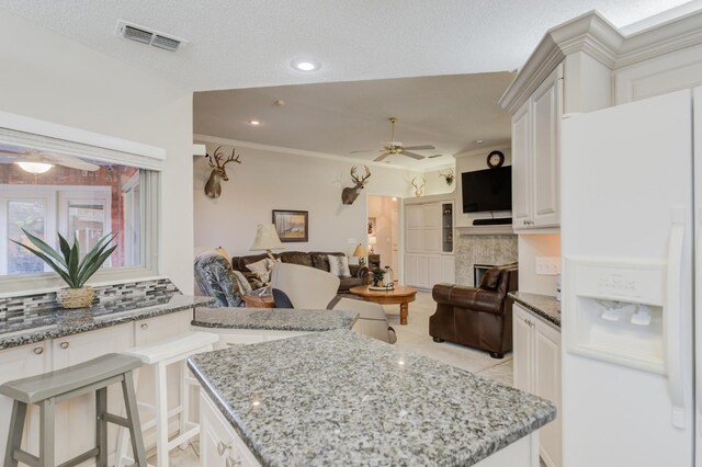 kitchen with white cabinetry, backsplash, white refrigerator with ice dispenser, and light stone countertops