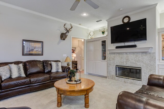 living room with crown molding, light carpet, a textured ceiling, a tile fireplace, and ceiling fan