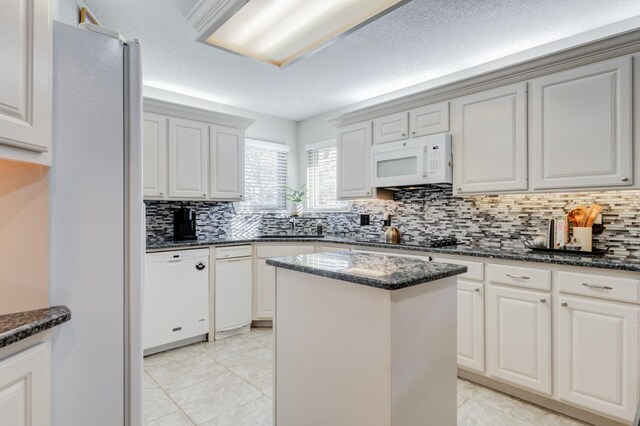 kitchen featuring white appliances, dark stone countertops, a kitchen island, and white cabinets